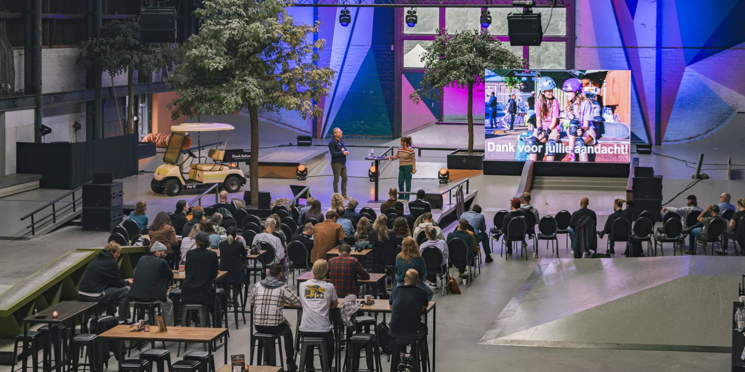 Grootschalige presentatie in de skatehal van Pier15 in Breda tijdens een zakelijk evenement met groot LED-scherm en publiek.