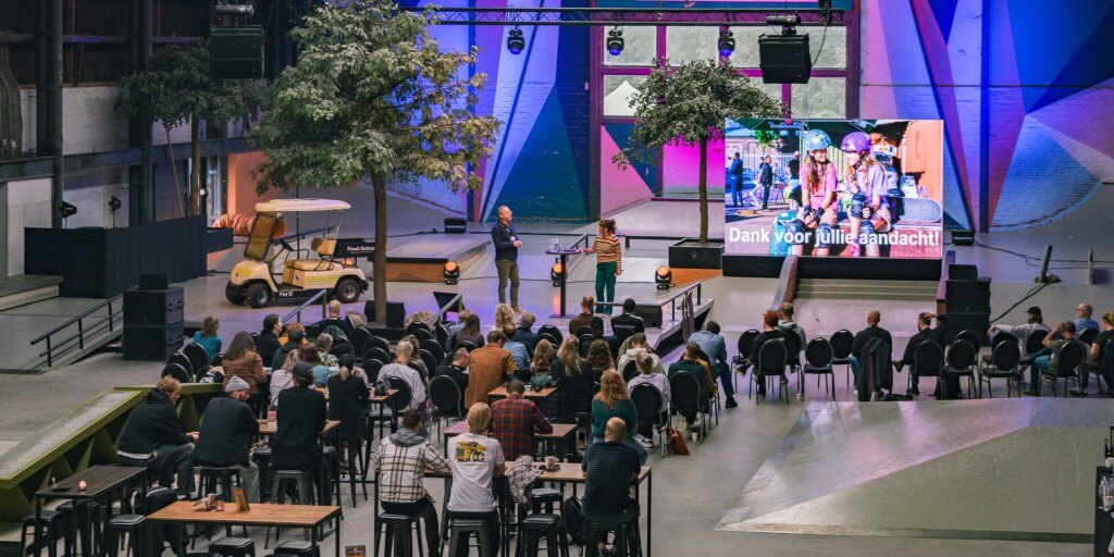 Grootschalige presentatie in de skatehal van Pier15 in Breda tijdens een zakelijk evenement met groot LED-scherm en publiek.